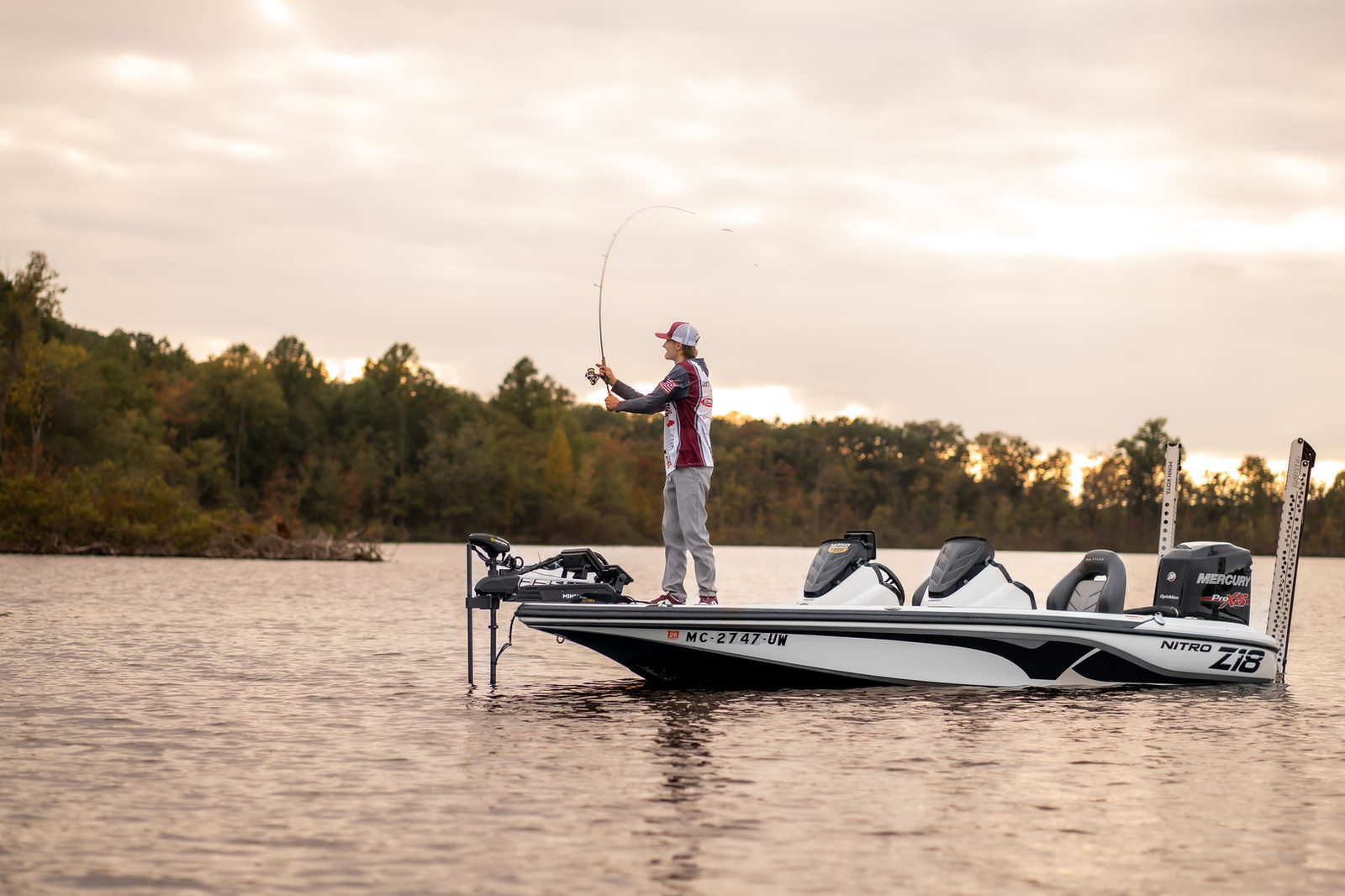 An angler casting from a Nitro bass boat at sunrise on a Michigan lake